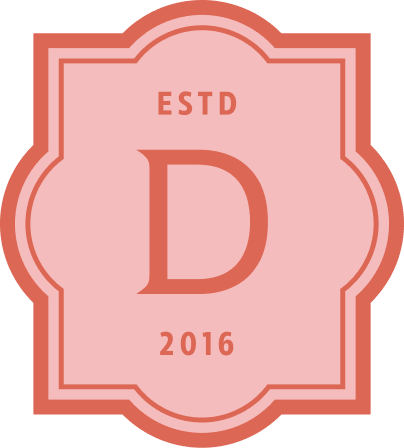 A pink and red emblem with a large letter 'D' in the center, ESTD at the top, and 2016 at the bottom, featuring a decorative border.