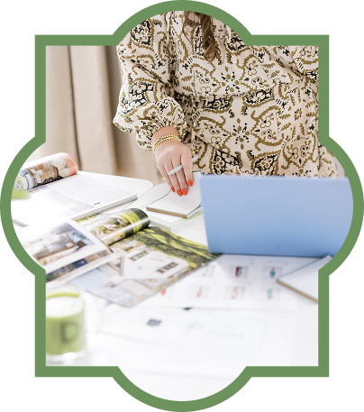 Person working at a desk with a laptop, open magazines, papers, and a mug.