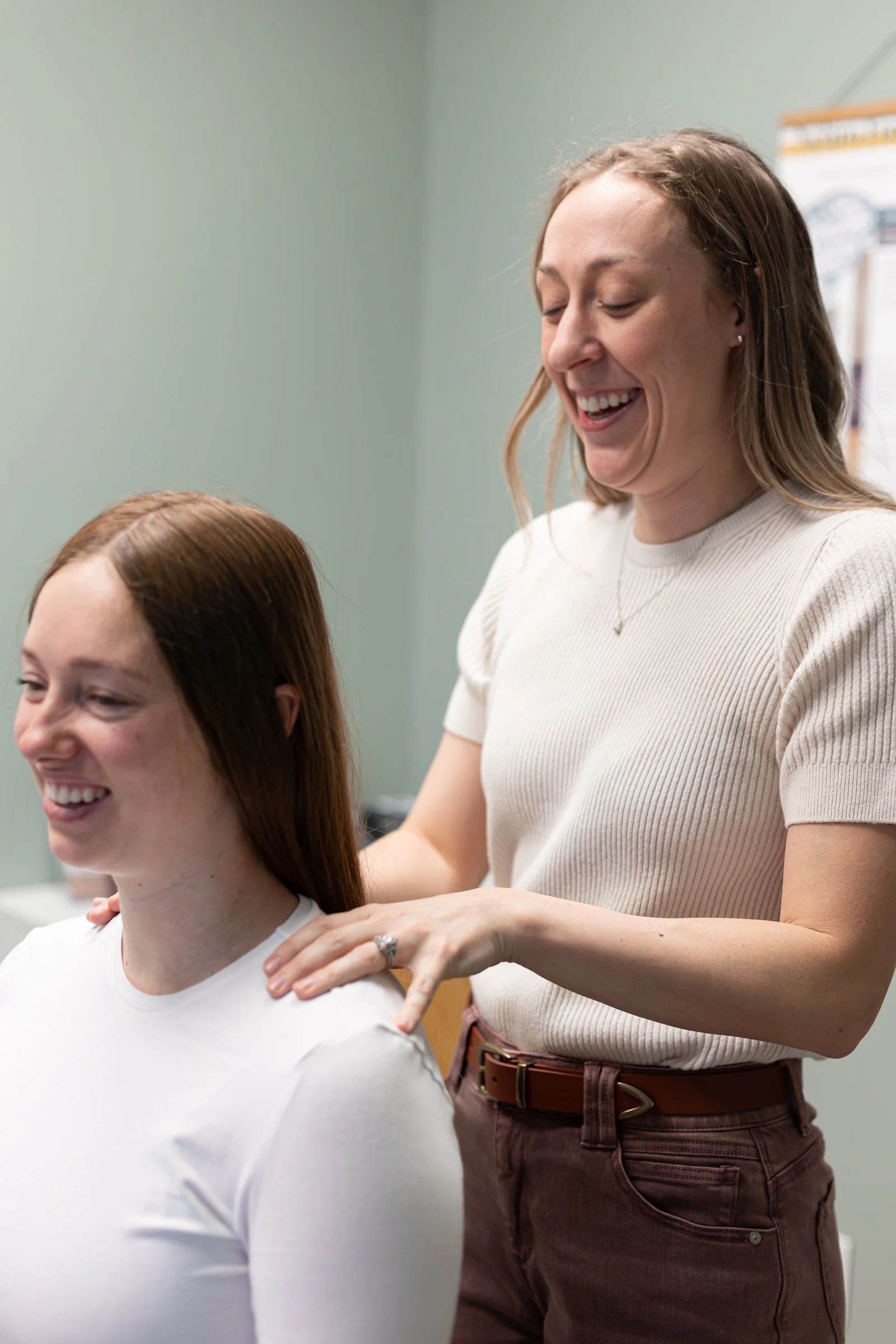 A hairstylist smiling while giving a shoulder massage to a client in a salon.