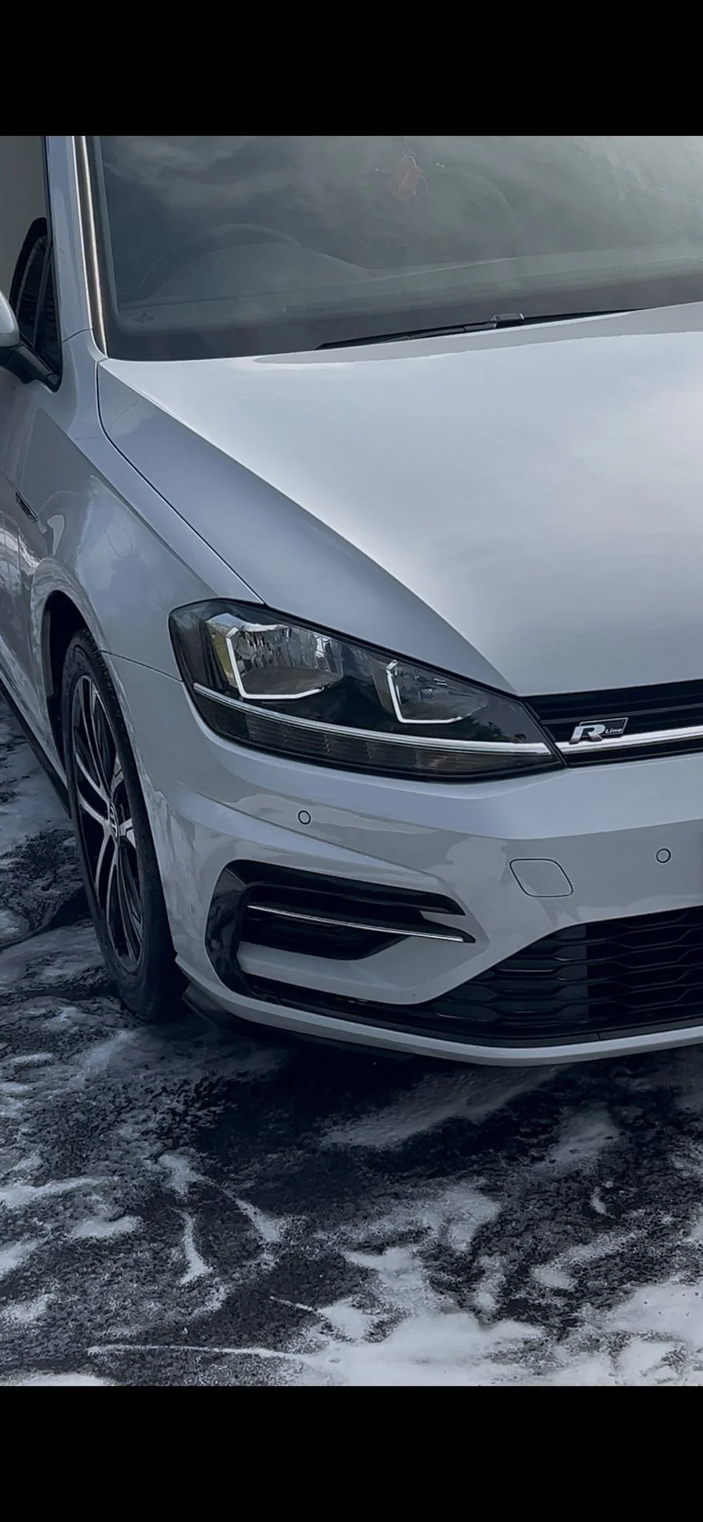 Front left side of a white Volkswagen R-Line car parked on a snowy surface.