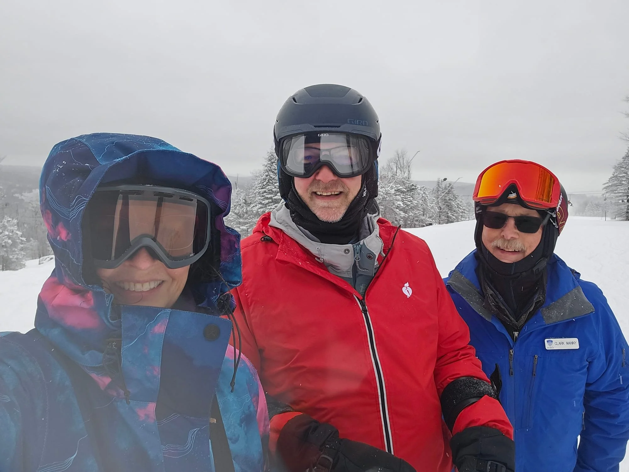Kittyhawk Ski Club members.  Three people dressed in winter gear and ski helmets taking a selfie in a snowy landscape with trees in the background