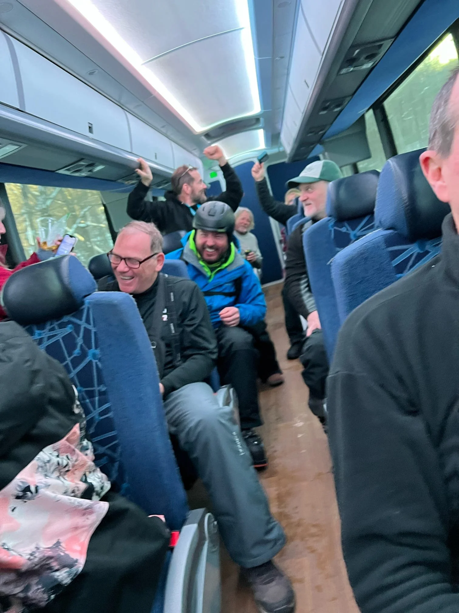 Kittyhawk Ski Club members.  A group of people sitting inside a bus, some are smiling, and two men are standing and raising their fists in celebration or excitement.