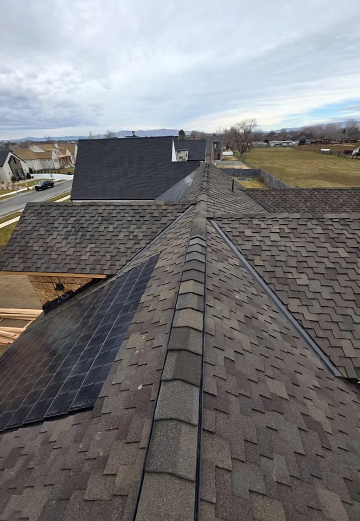 Aerial view of rooftops with solar panels, shingles, and a backyard in a suburban neighborhood.