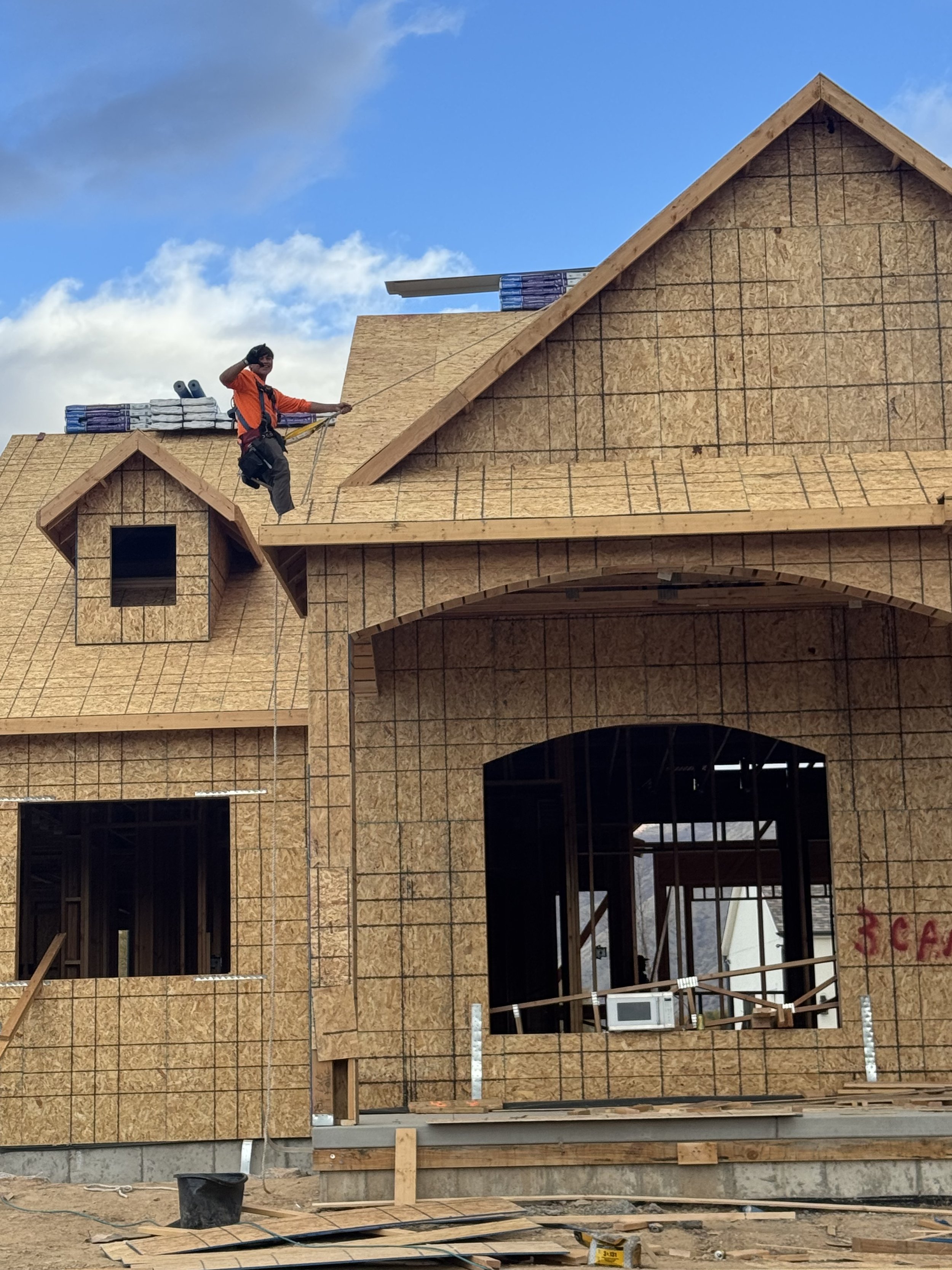 Construction worker on a roof of a house under construction, with a partly cloudy sky in the background.