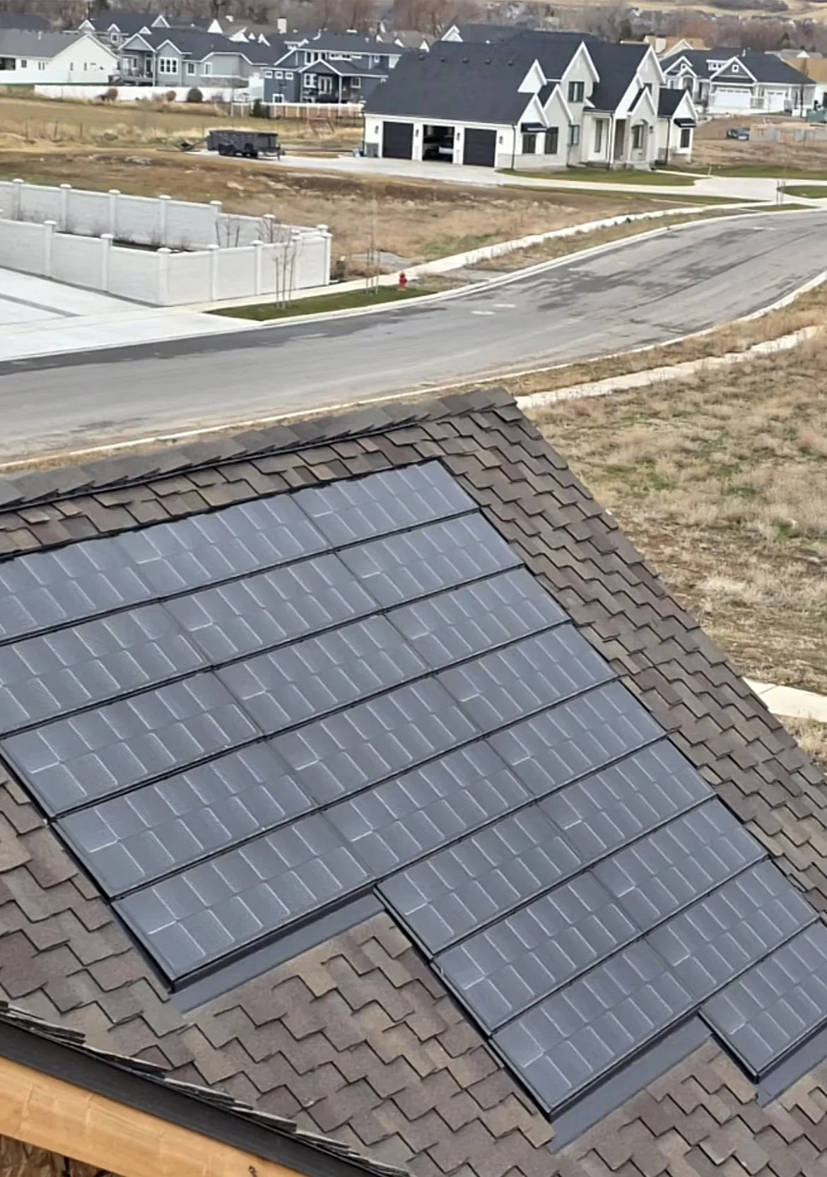 Solar panels installed on a brown shingled roof in a residential neighborhood.