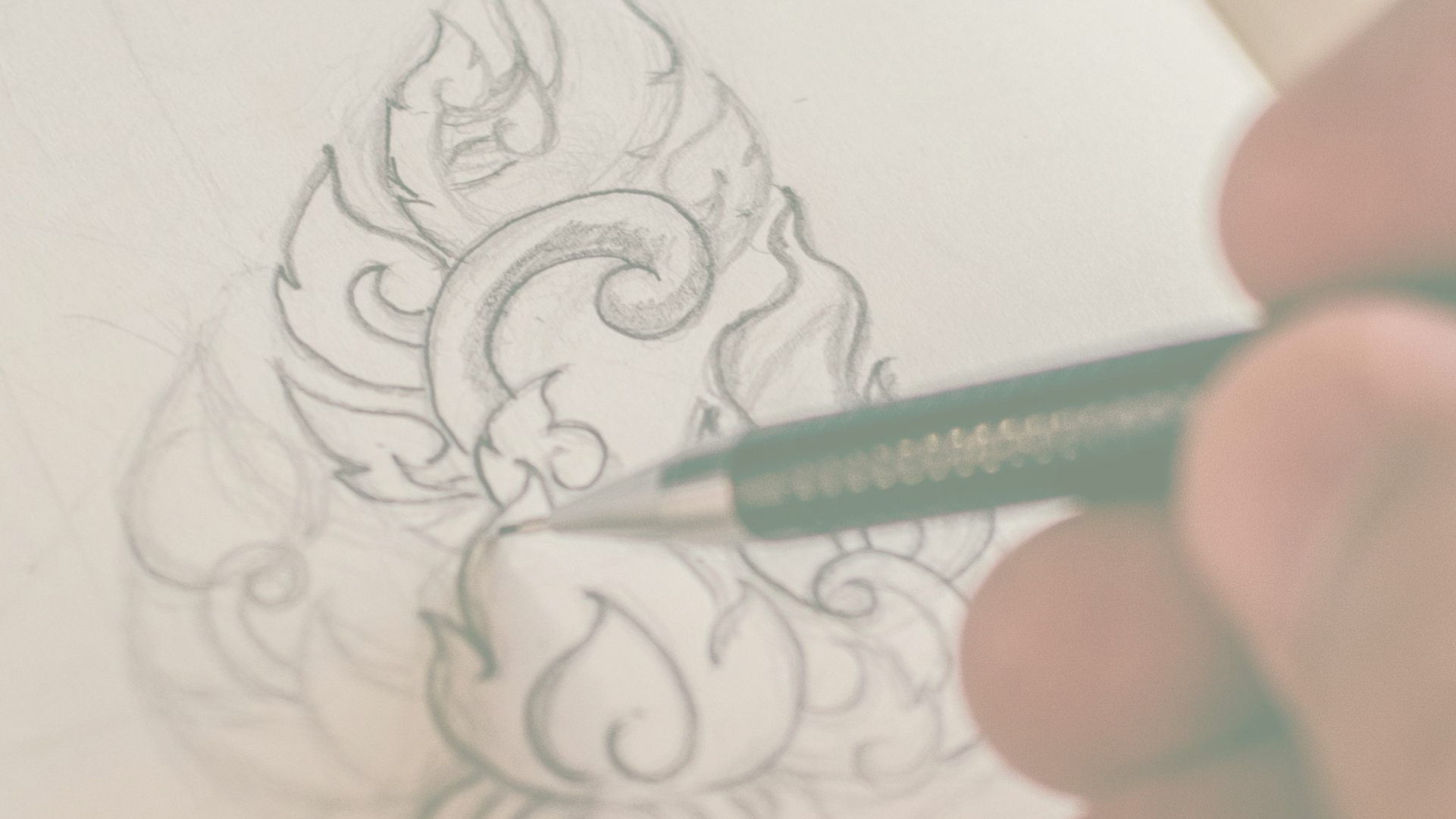 A person drawing a ornate decorative design with a pencil on paper.