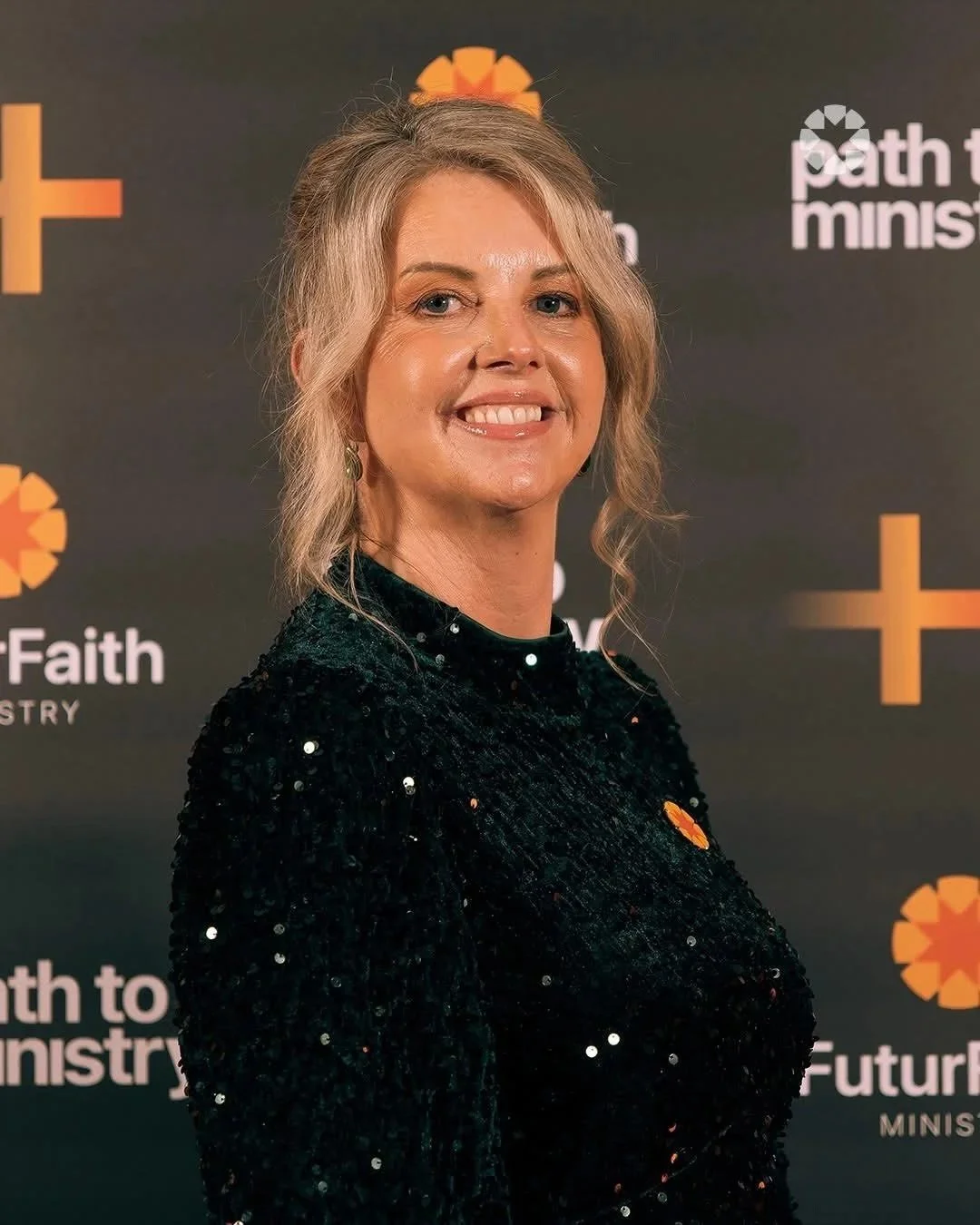 A woman with blonde hair, wearing a black sequined dress, smiling, standing in front of a backdrop with religious symbols and the words 'Path to Ministry' and 'Future Faith'.