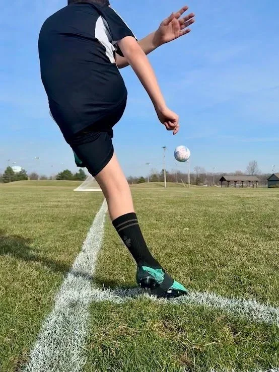 A soccer player kicking a ball on a field during daytime.