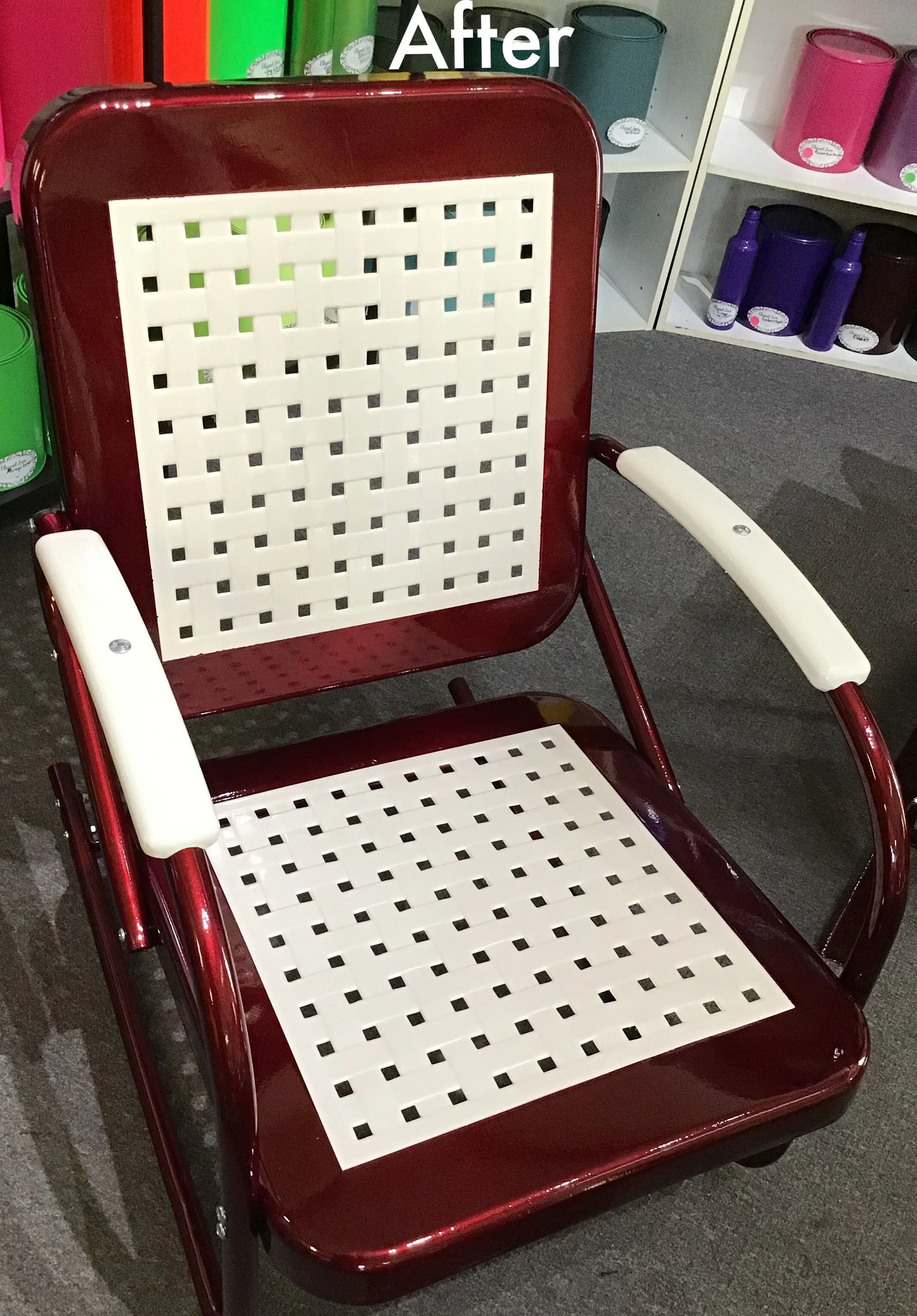 A red metal chair with white vinyl-wrapped armrests and a white slotted backrest and seat, positioned in front of a display of colorful paint cans.