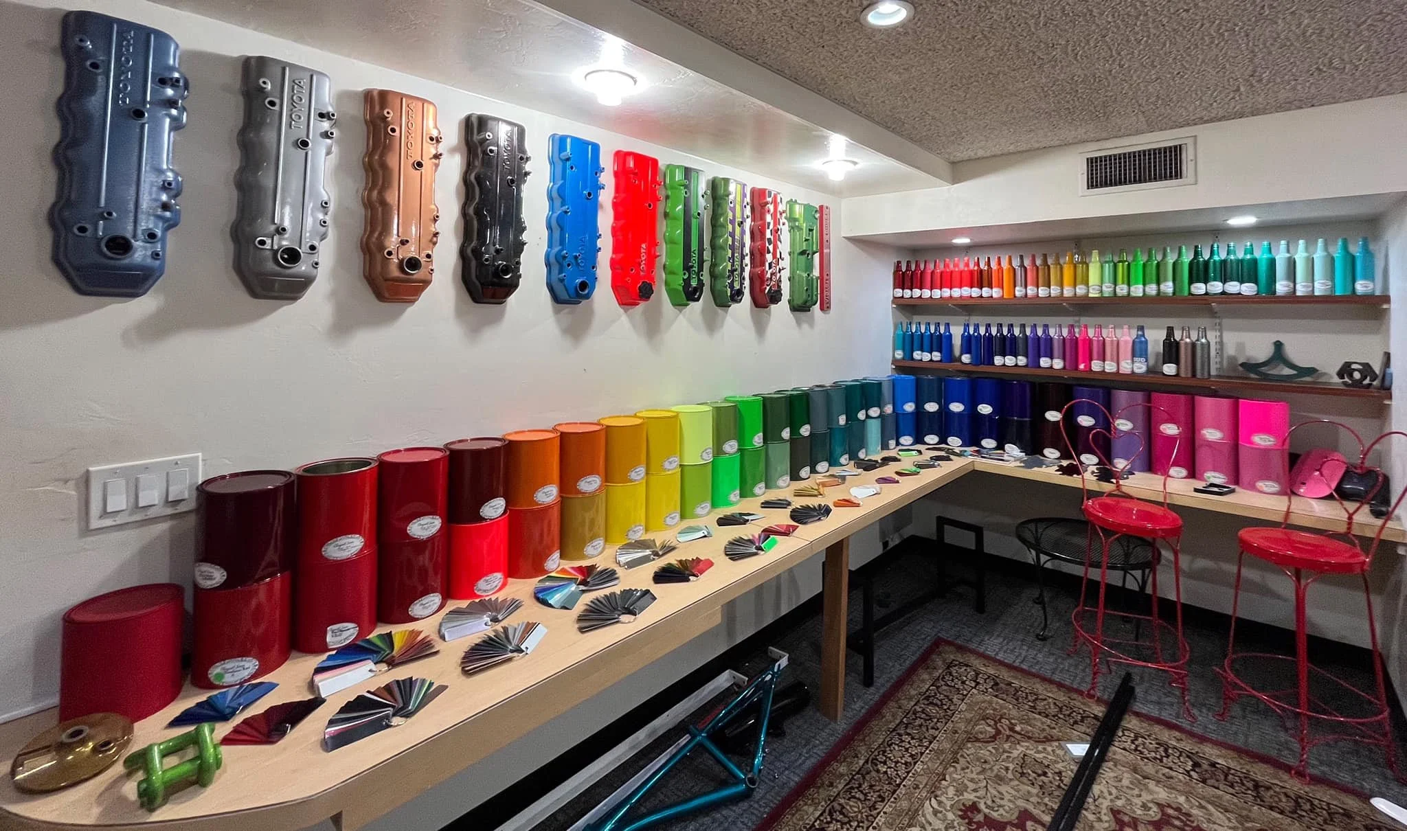 A room displaying automotive paint color samples and paint spray cans on shelves and a table, with paint color swatches and bottles organized in a rainbow order.