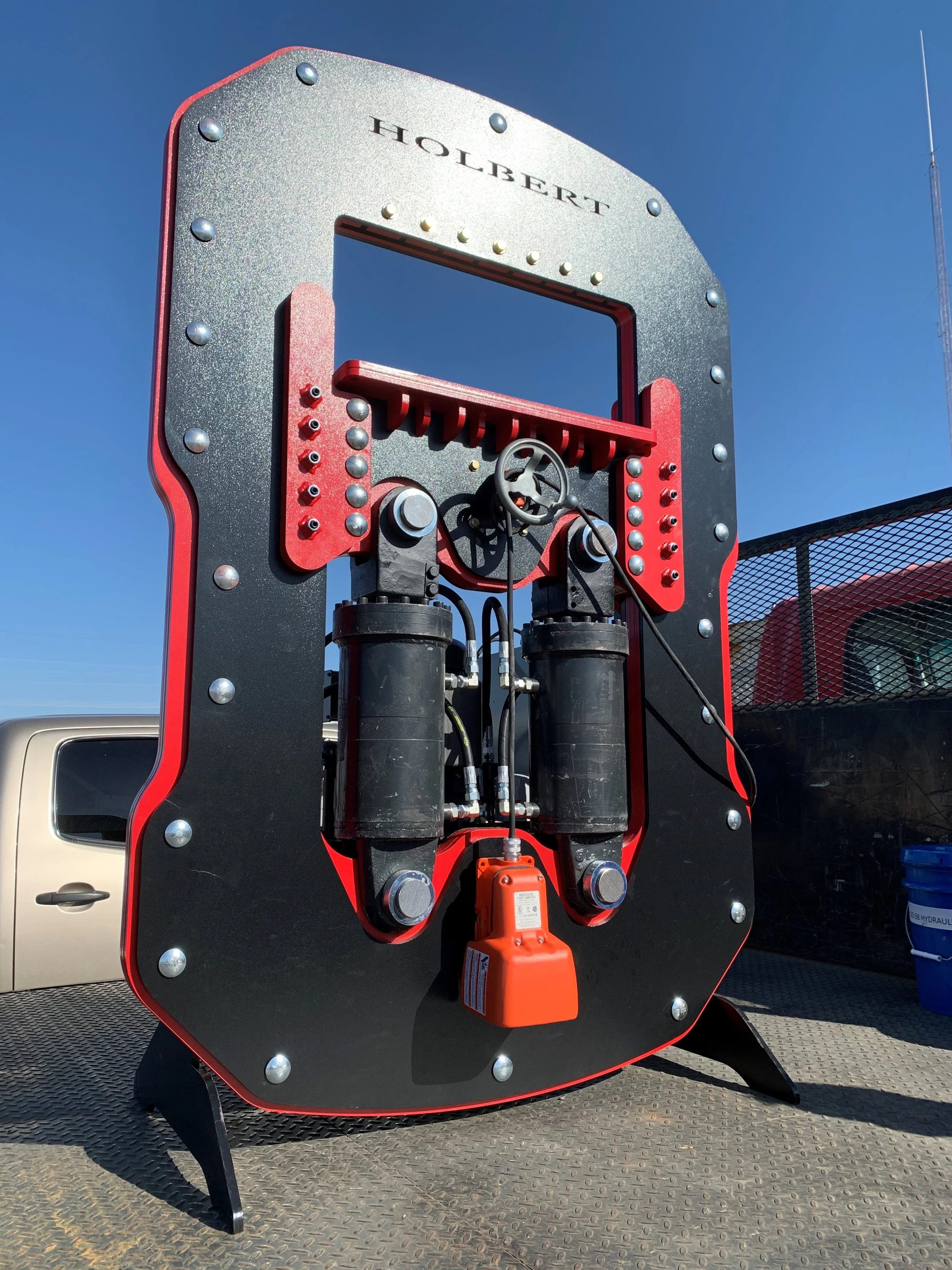 Large mechanical device labeled 'Holbert' with hydraulic components and a steering wheel, set outdoors against a blue sky.