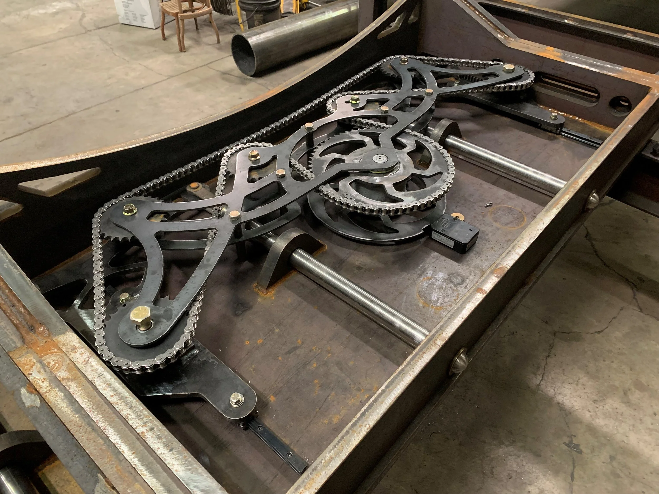 A metal bicycle chain and sprockets on a work table in a workshop.