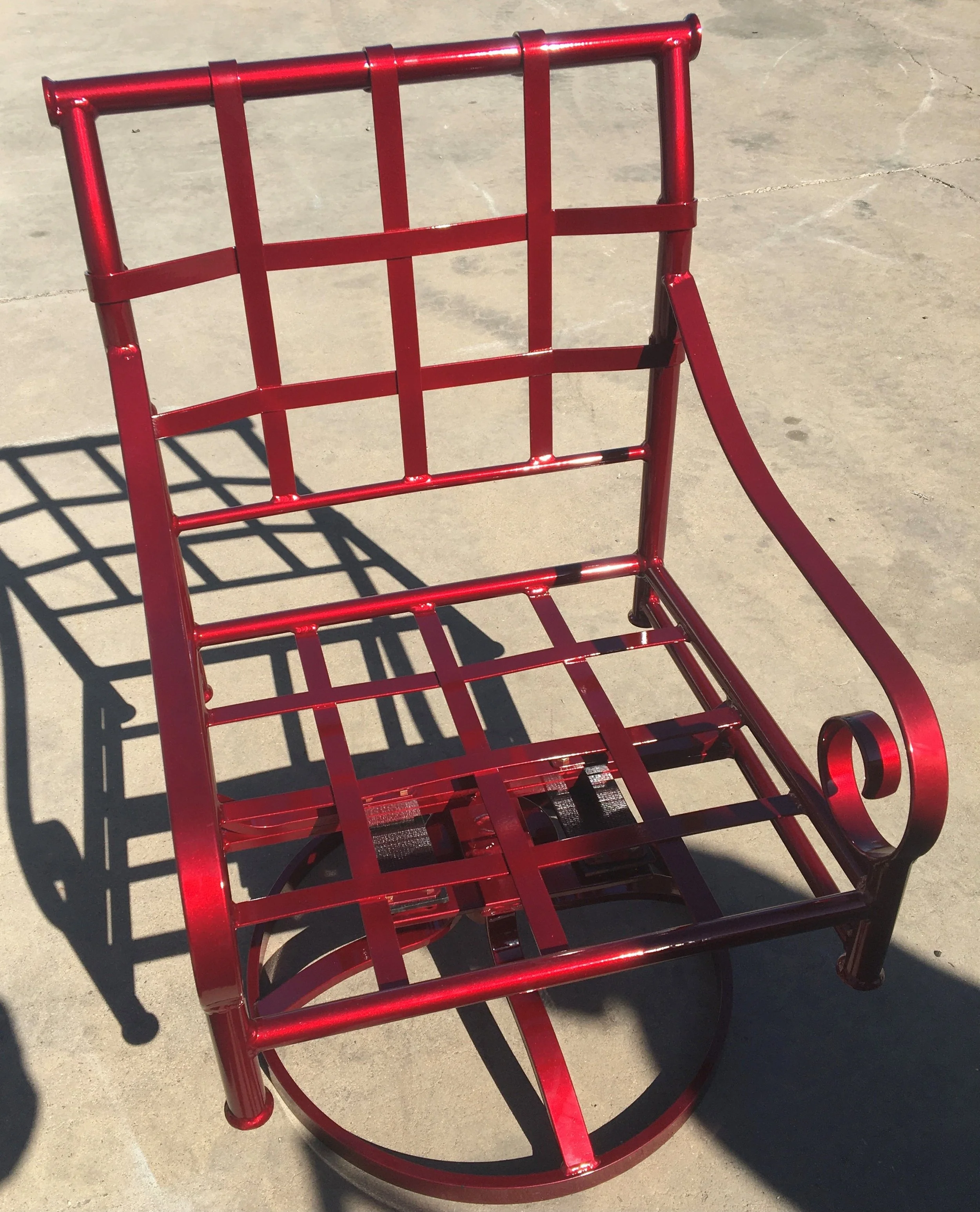 Red metal garden cart with a lattice pattern, casting shadow on concrete ground under sunlight.