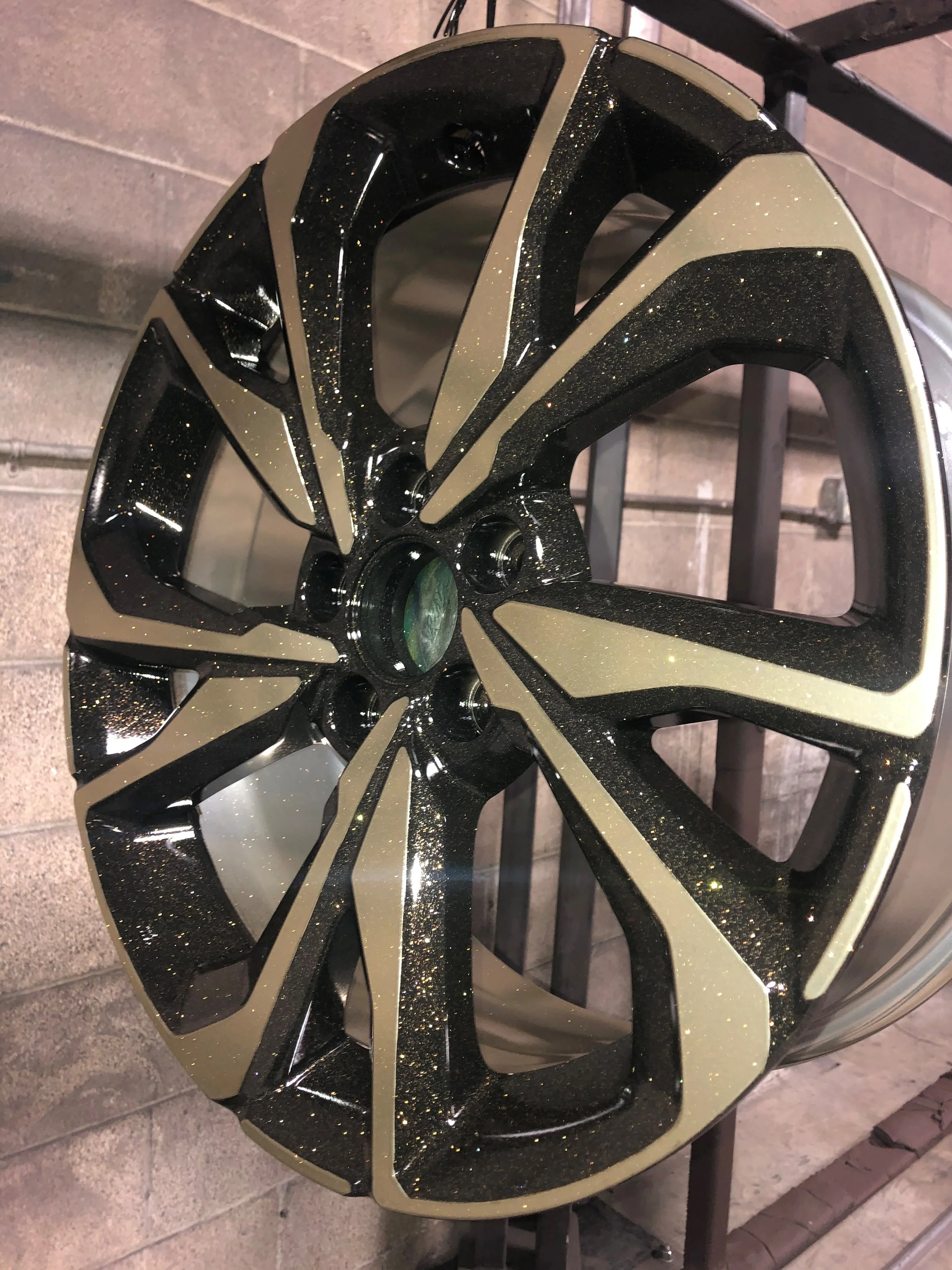 A close-up view of a car wheel rim with black and gold accents and a glittery finish, mounted on a vehicle.