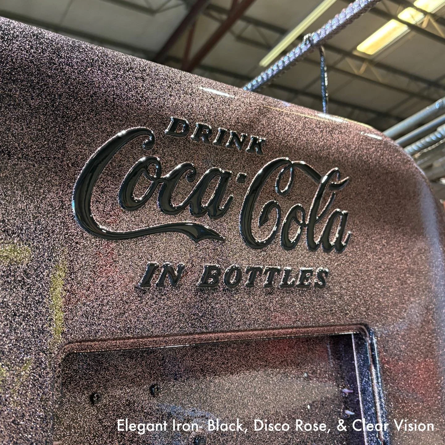Close-up of a vintage Coca-Cola vending machine with a speckled, glittery finish in disco rose color, featuring black embossed text that reads 'Drink Coca Cola in Bottles'.