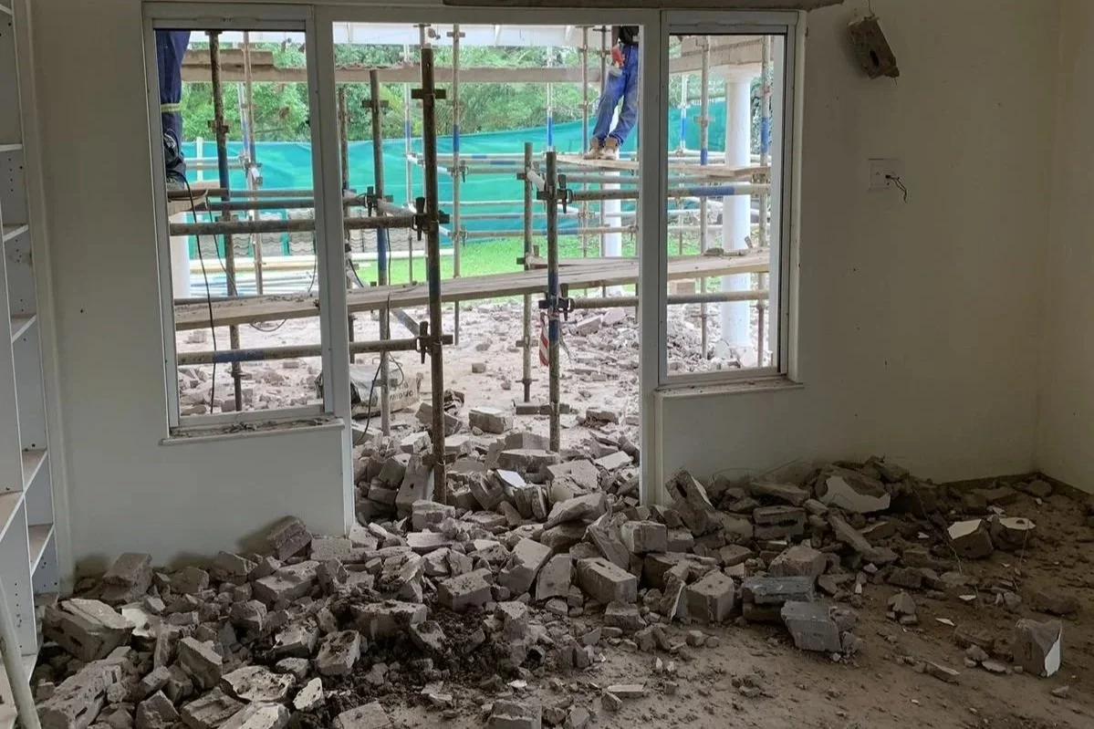 Construction site with broken bricks and rubble inside a building, with scaffolding visible outside the window.