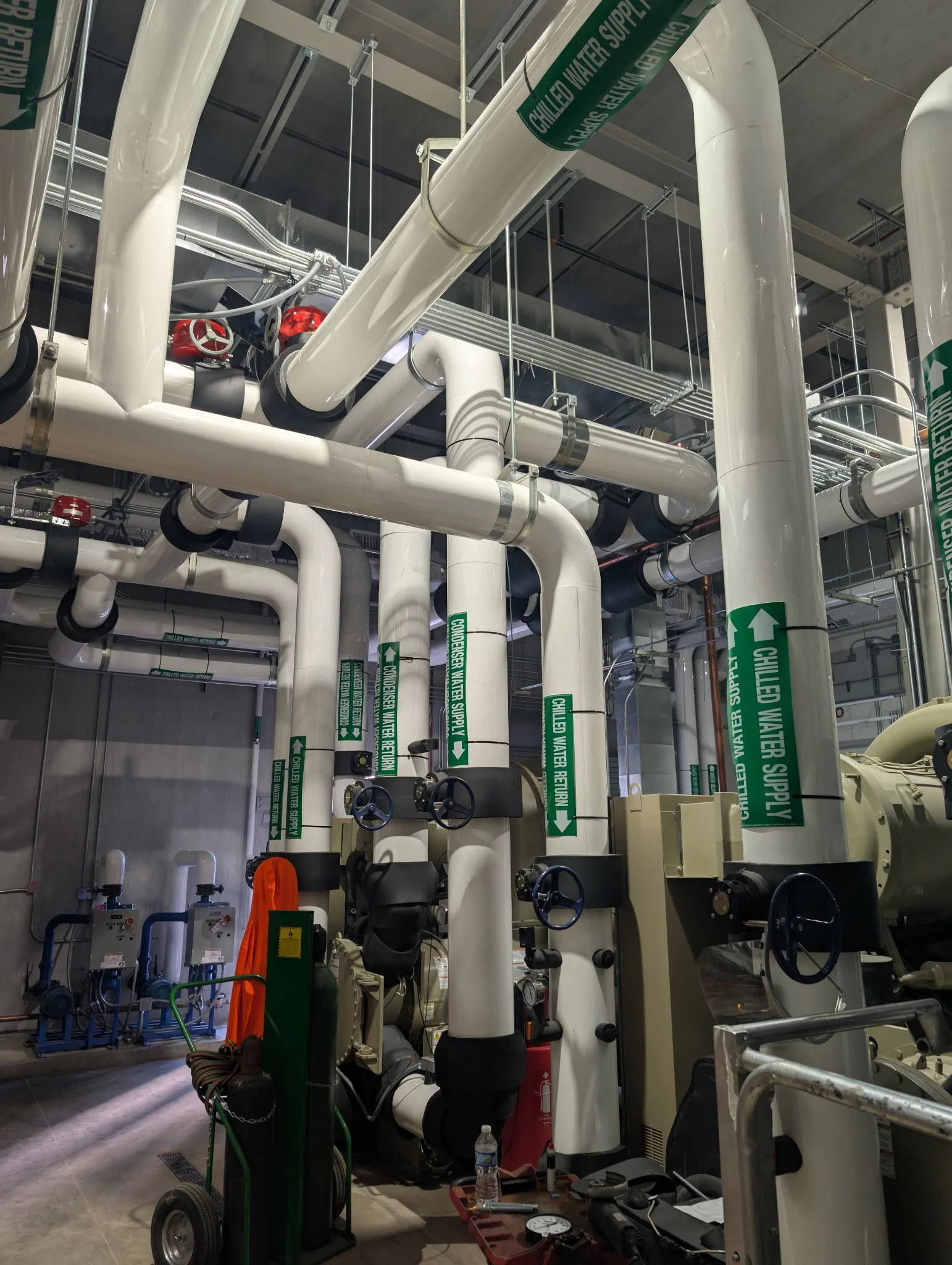 A complex system of white pipes and valves in an industrial setting, with labels indicating water supply and return, along with electrical equipment and tools.
