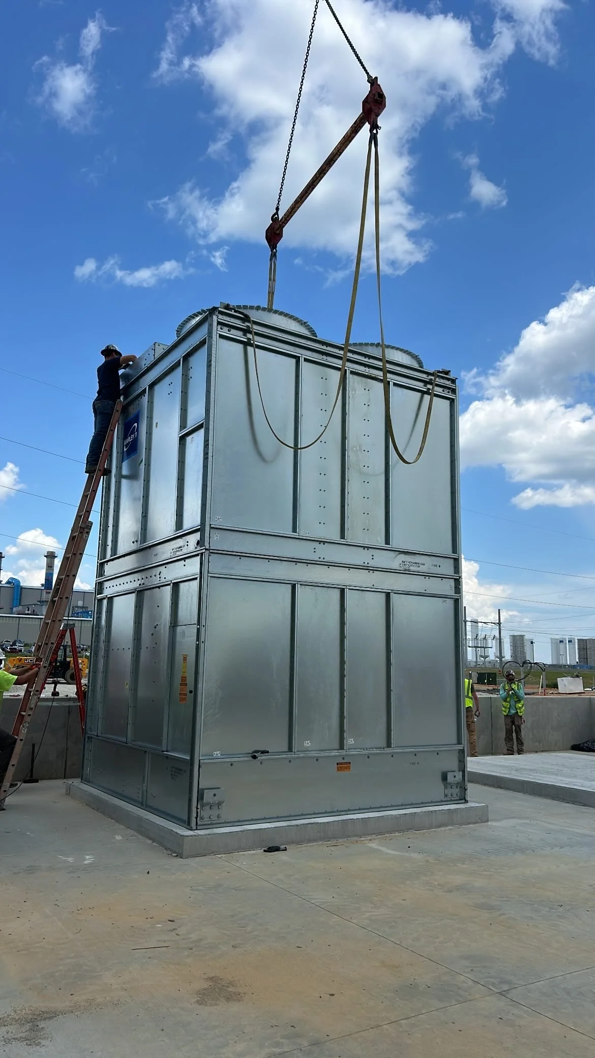 Construction workers installing a large industrial HVAC unit with a crane on a construction site.
