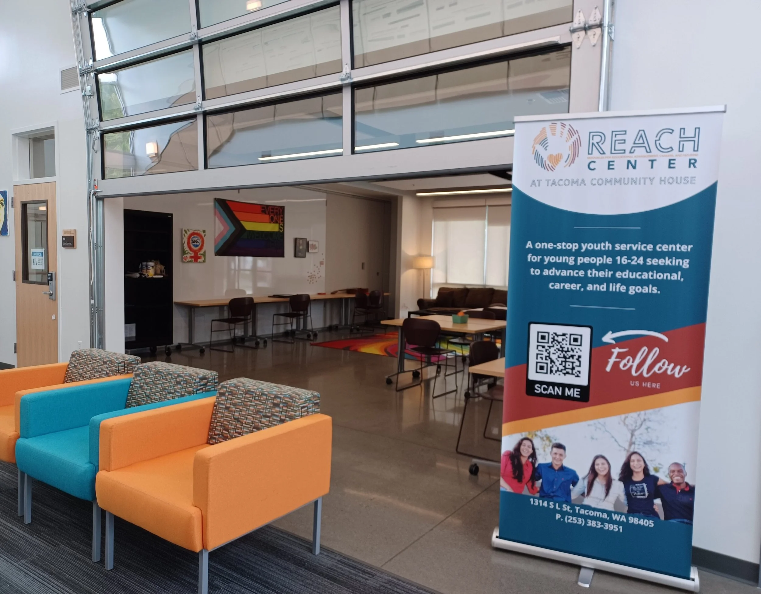 Interior of a community youth center with colorful seating, tables, chairs, and a REACH Center banner promoting youth services at Tacoma Community House.