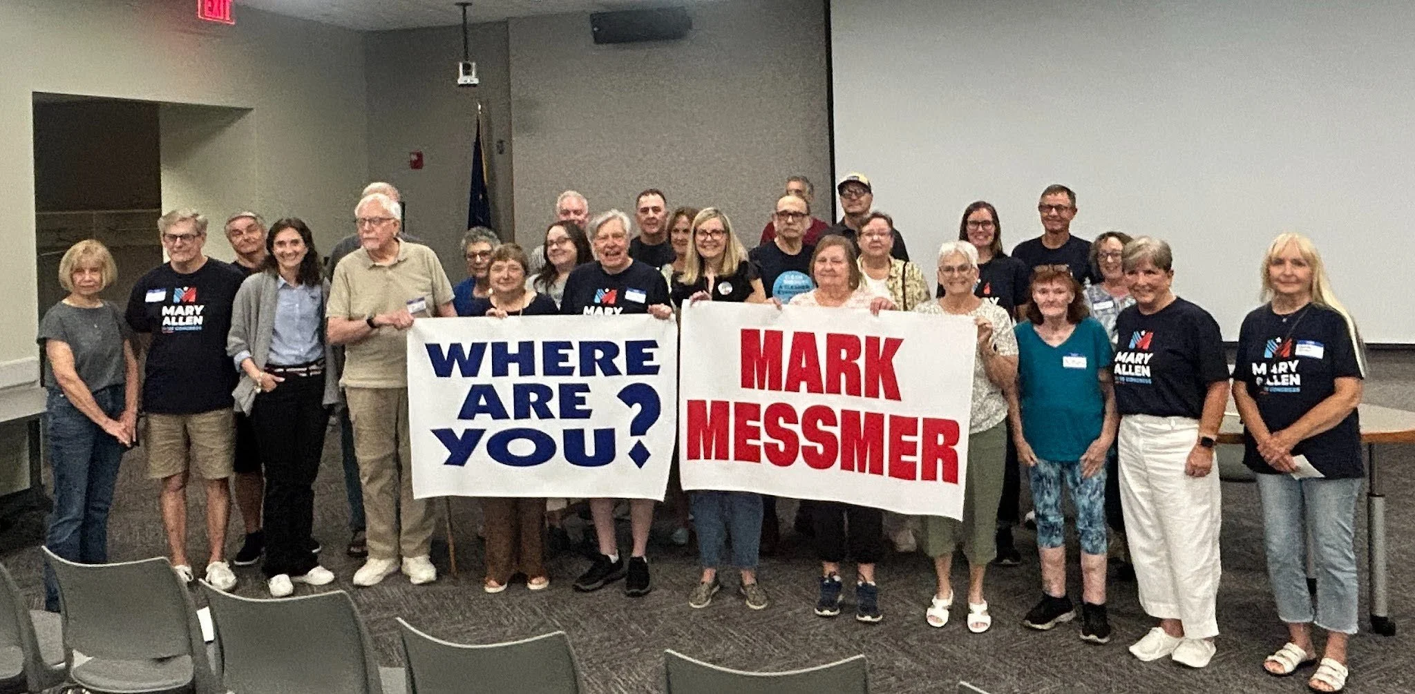 Town Hall attendees pose for a group photo with posterboards reading "Where are you Mark Messmer?"