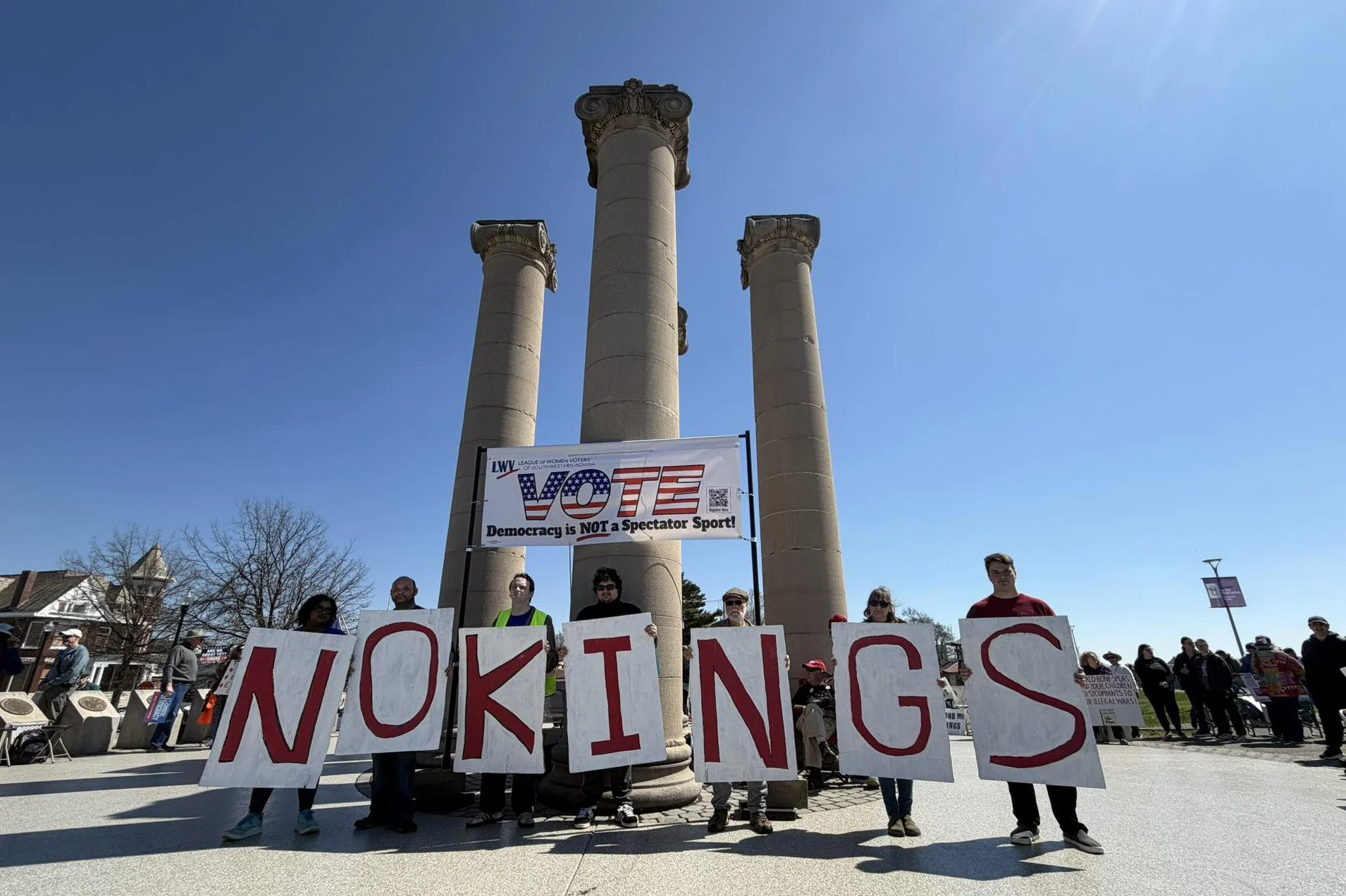 7 protestors in front of the Four Freedoms monument in Evansville holding signs that spell "No Kings"