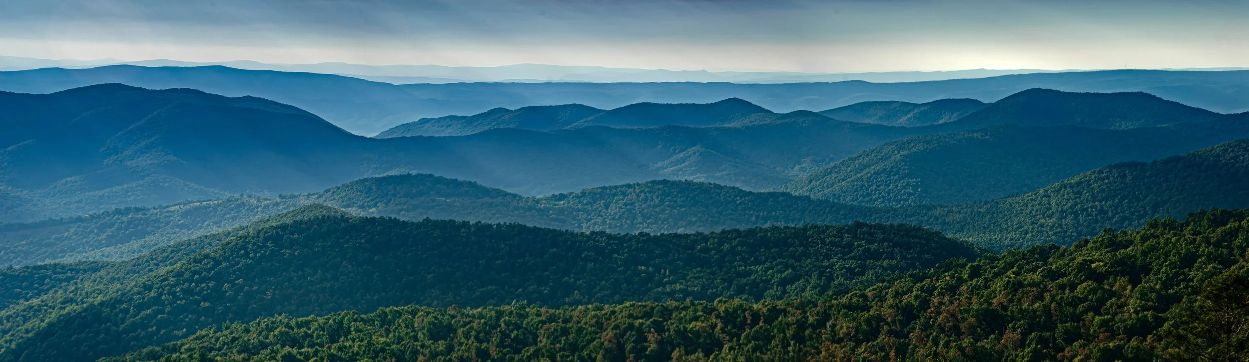 A panoramic view of rolling green mountain ranges under a cloudy sky.