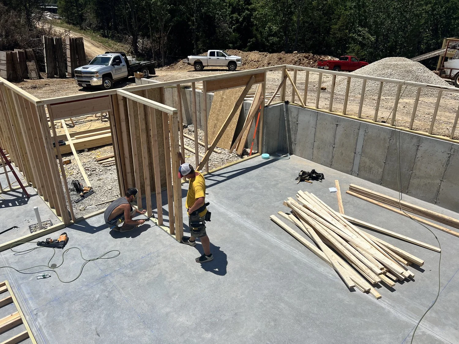 Two construction workers building a wooden frame on a concrete foundation at a construction site.