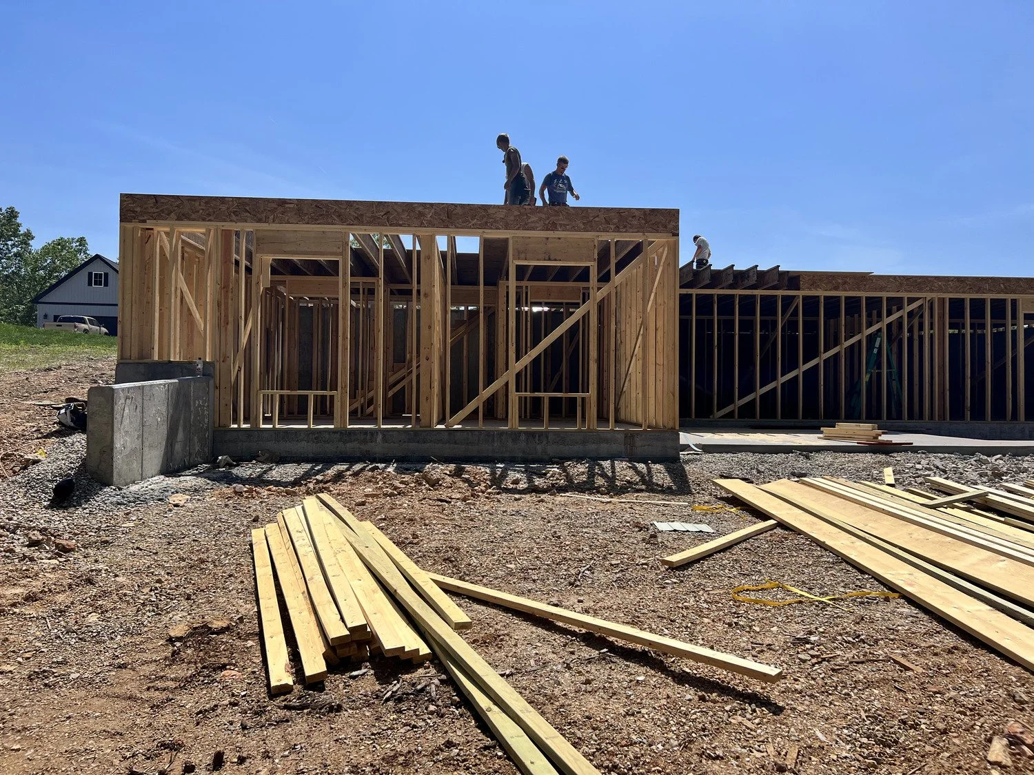Construction site with wooden framing for a building, several workers on the roof, and building materials scattered on the ground.
