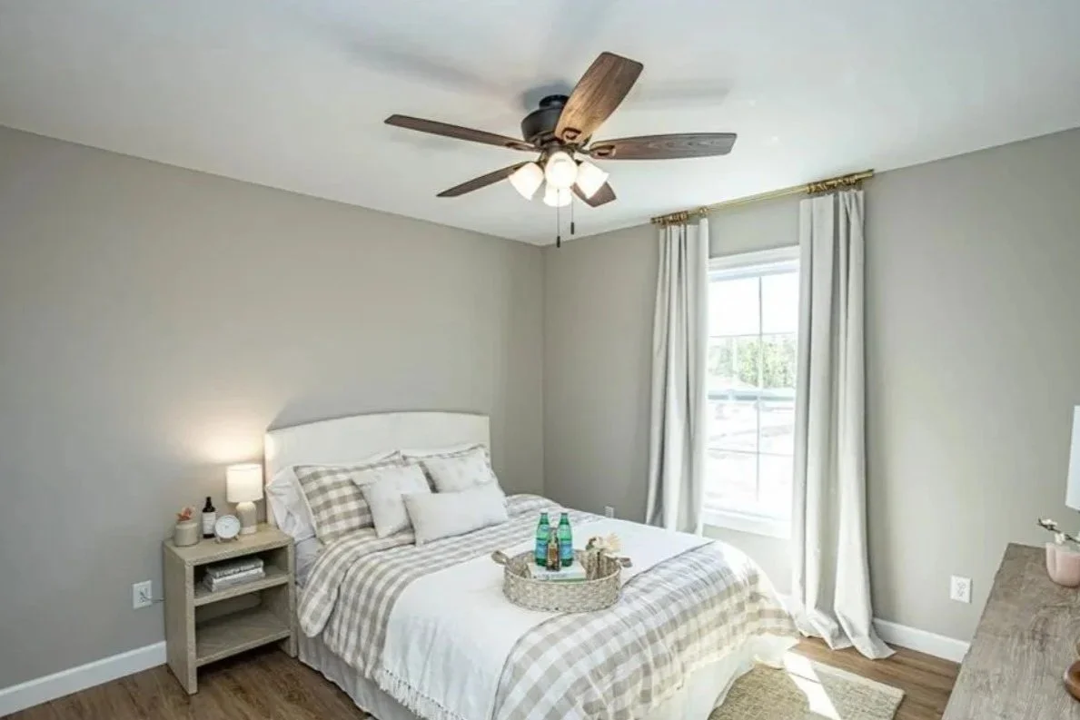 A bedroom with a bed, nightstand, window, curtains, ceiling fan, and dresser.