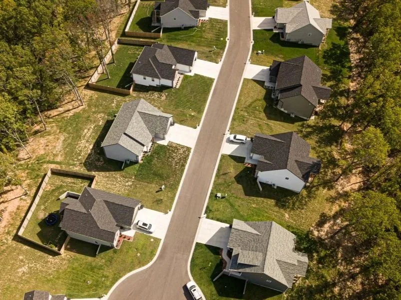 Aerial view of suburban houses with driveways, on a curved street, surrounded by trees.