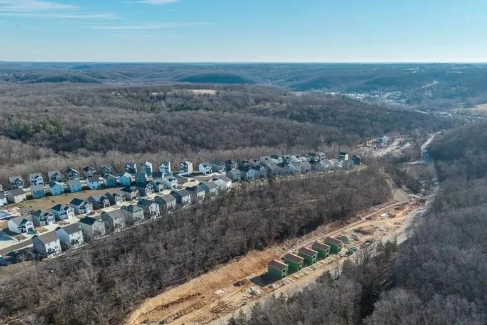 Aerial view of a residential neighborhood with new construction homes and a wooded area undergoing development in a valley.