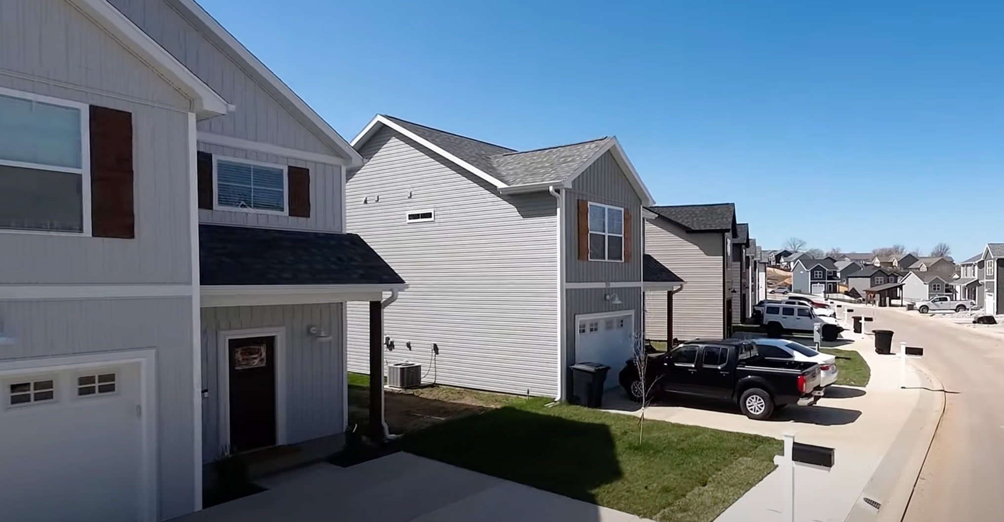 A suburban street with modern townhouses, parked cars, and a clear blue sky.