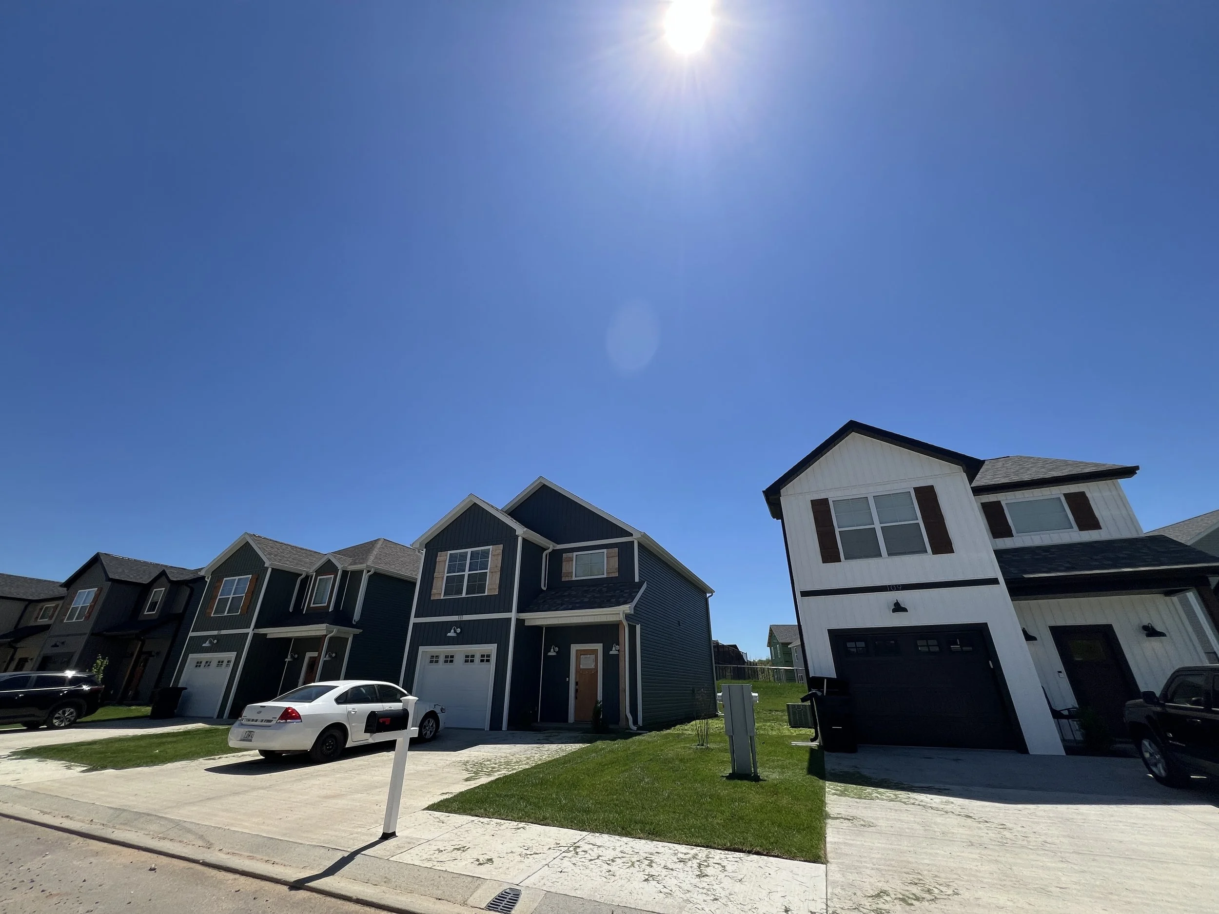 A row of modern, two-story houses with garages, seen under a clear blue sky with the sun shining brightly.