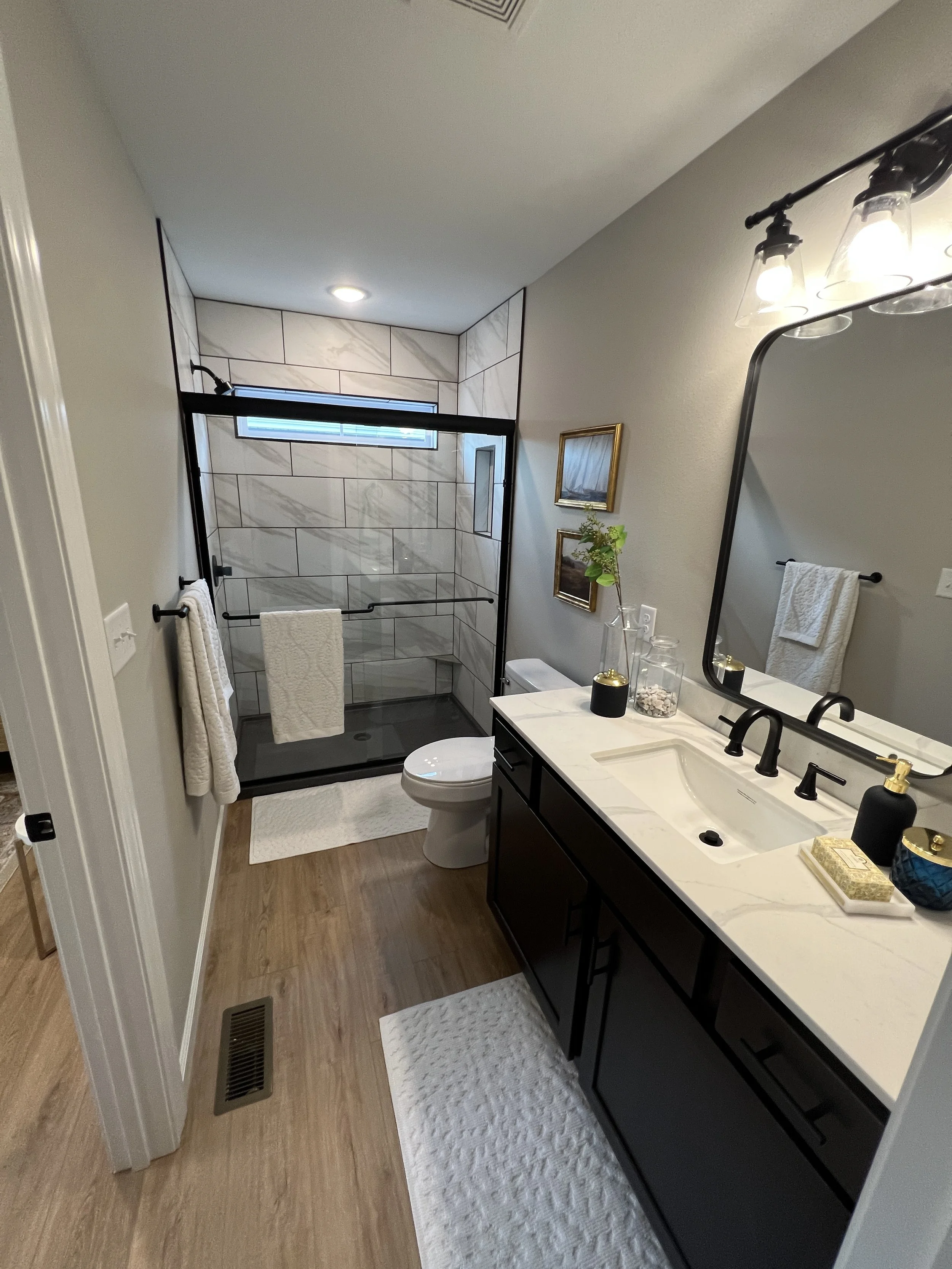 Bathroom with a glass shower, white marble vanity with black cabinets, mirror, and towel racks.