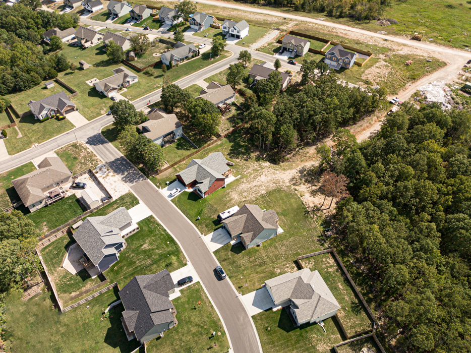 Aerial view of a suburban neighborhood with houses, lawns, trees, and some construction areas.