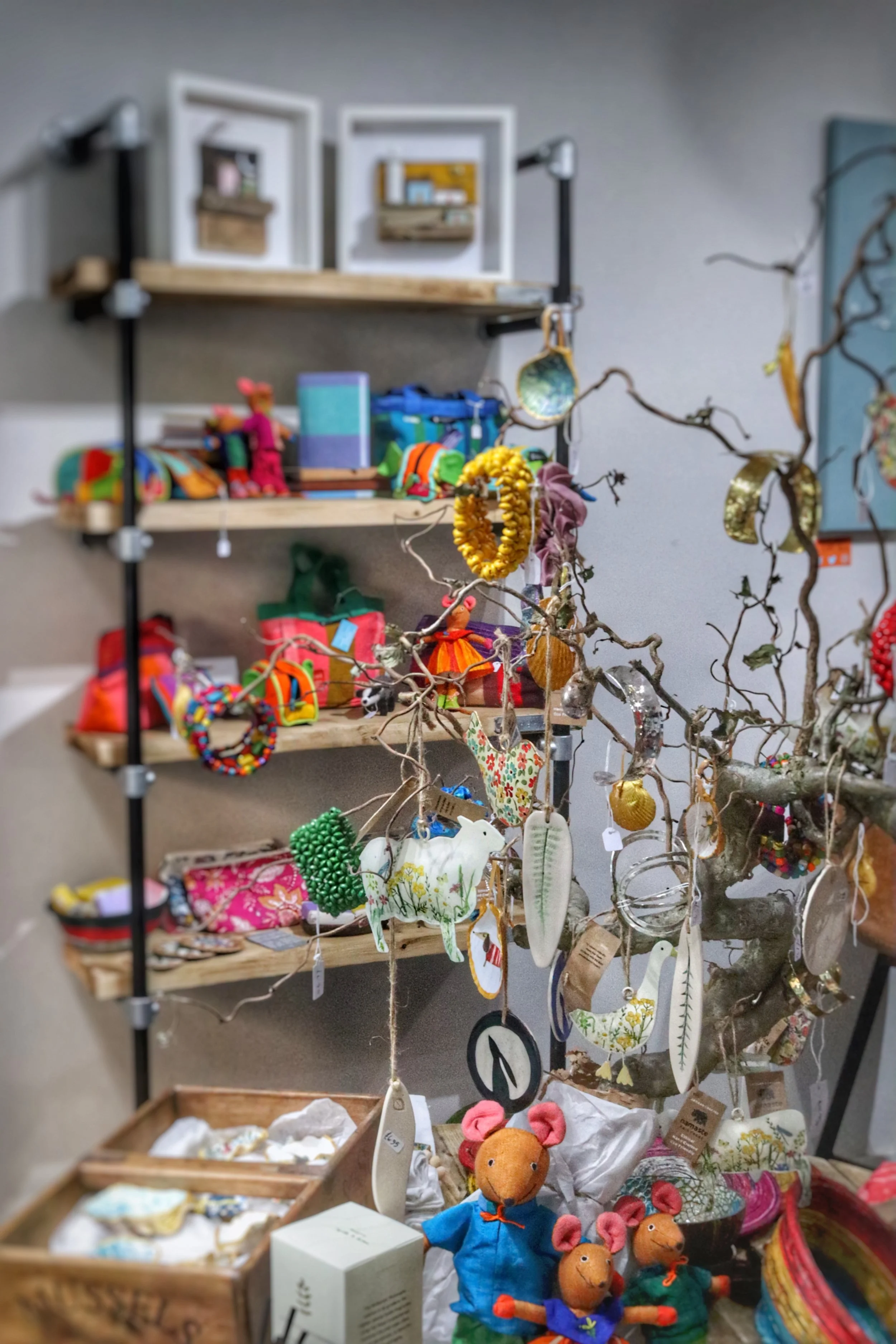 Display of handmade crafts, including stuffed animals, ornaments, and decorative items on wooden shelves and a branch, in a craft store or market.