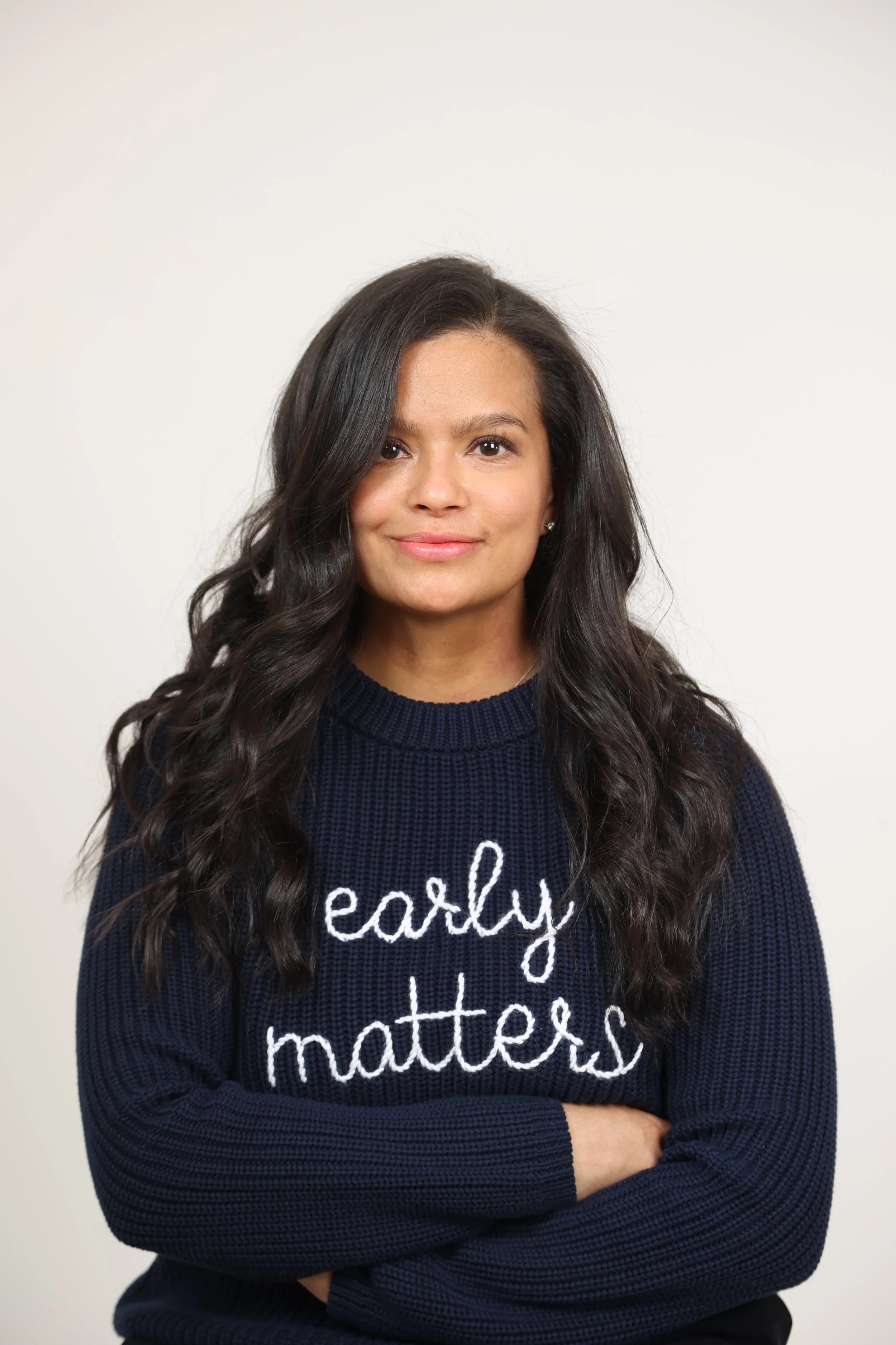 image of founder (brunette woman) wearing a navy blue sweater embroidered with "early matters" in white cursive