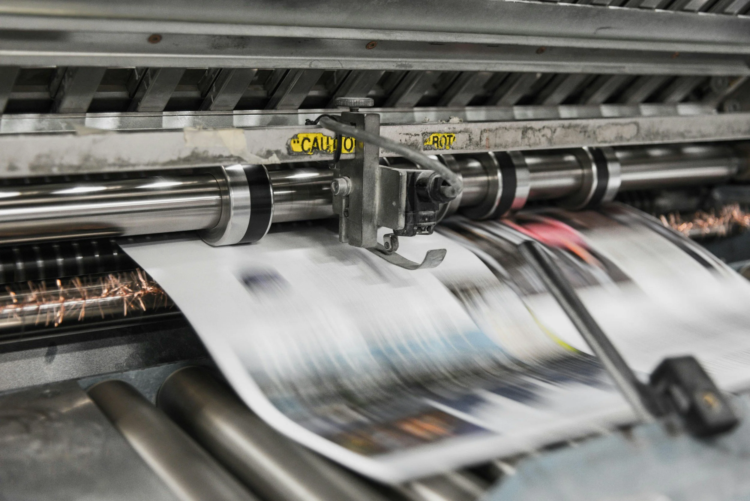 Close-up of a printing press with paper moving through rollers to print magazines or newspapers.