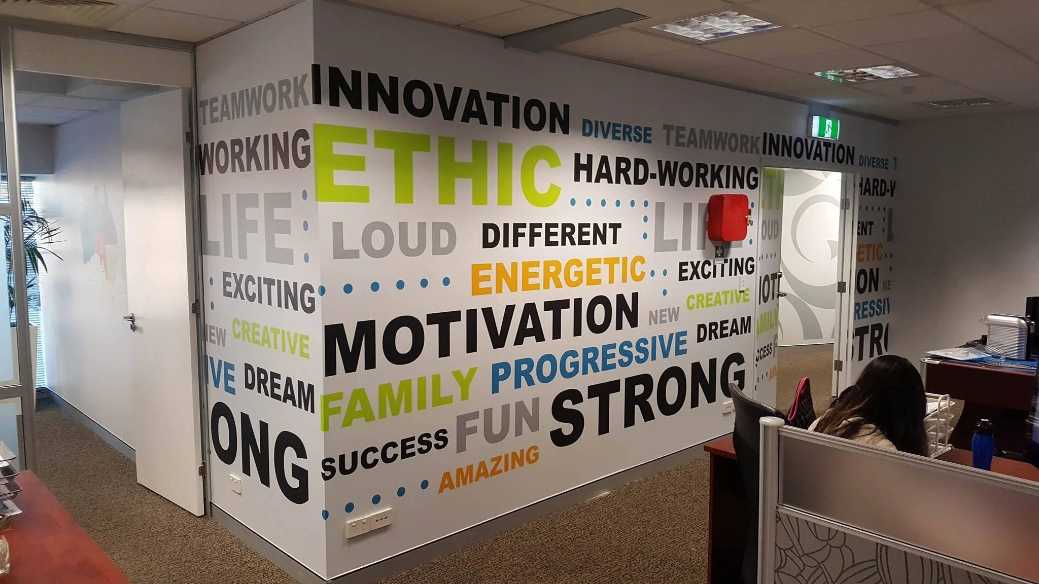 Office wall with words related to motivation, teamwork, innovation, diversity, and creativity in various colors and sizes.