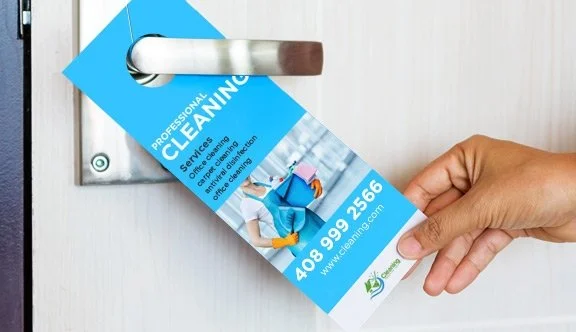 A person's hand pulling a blue and white cleaning service door hanger off a door handle.