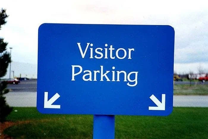 Blue sign indicating the direction to visitor parking with arrows pointing to the lower left.