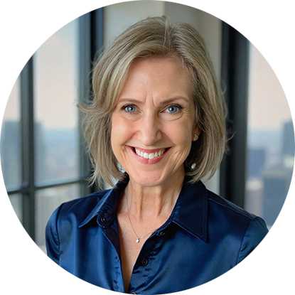 Smiling woman with short blonde hair in a dark blue blouse stands in a bright room with large windows showing a cityscape in the background.