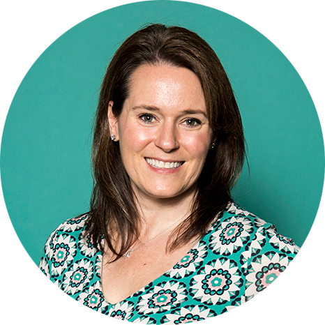 Smiling woman with brown hair, wearing a patterned teal and black blouse, against a solid teal background. The mood is friendly and approachable.