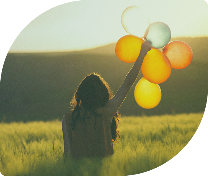 A girl holding colorful balloons in a field at sunset