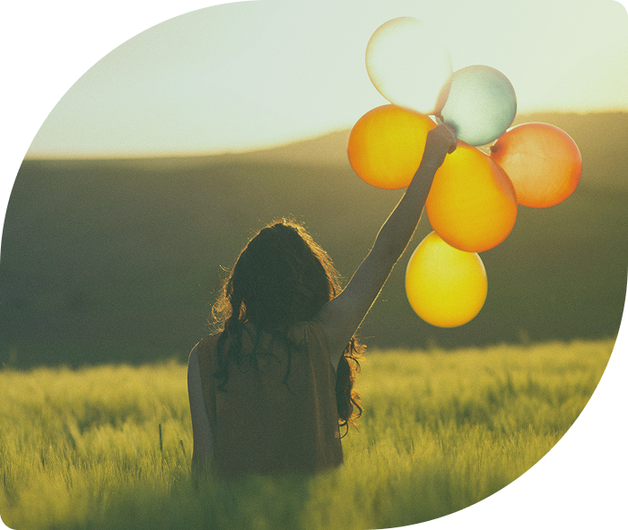 A girl holding colorful balloons in a field at sunset