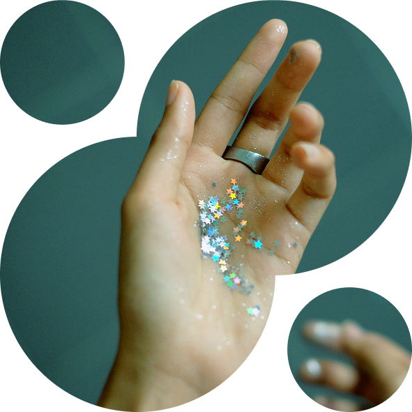 A hand with a silver ring holds multicolored star-shaped glitter, set against a teal background. The scene conveys a whimsical, magical vibe.