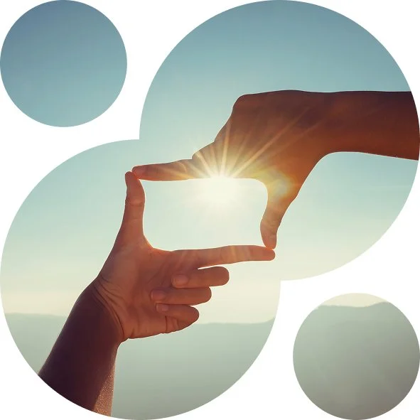 Two hands forming a rectangular frame around the sun with a mountain landscape in the background.