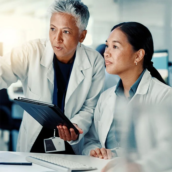 Two scientists in white lab coats reviewing information on a tablet together in a laboratory setting