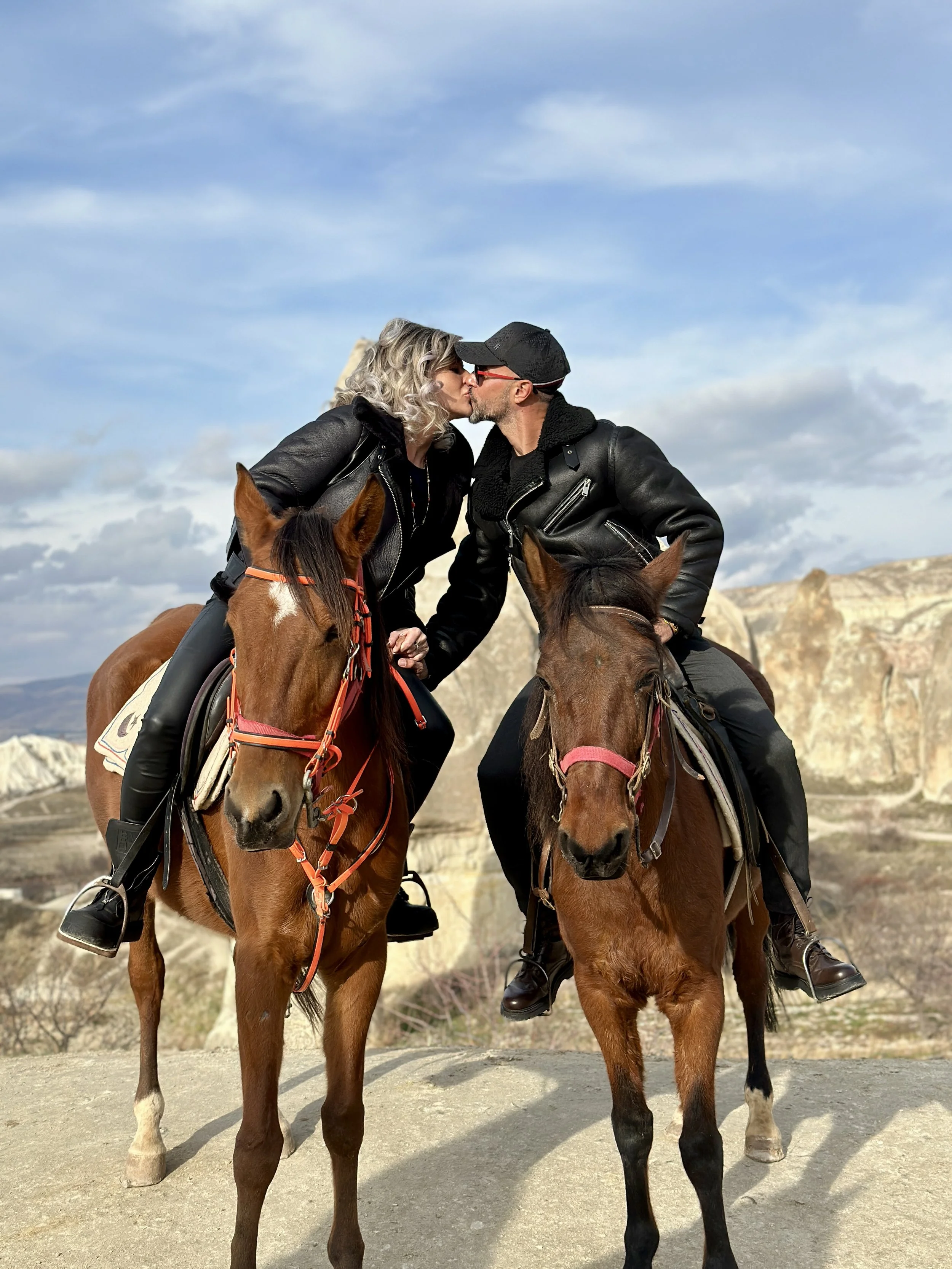 A couple riding horses in a scenic rocky landscape, sharing a kiss while sitting on their horses.