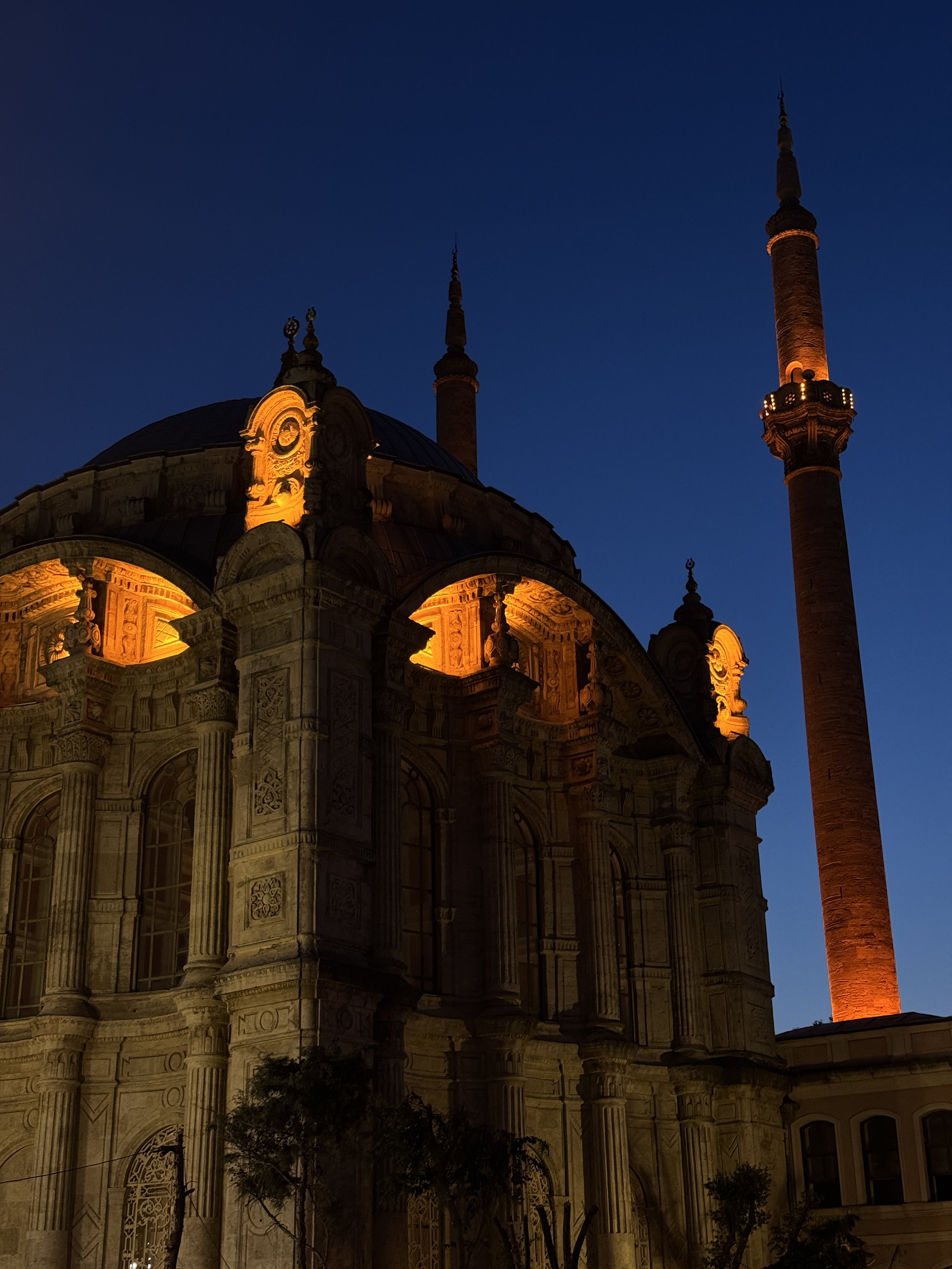 A historic mosque with illuminated architecture and tall minarets against a dark blue evening sky.